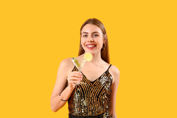 Beautiful young woman with glass of tasty martini on yellow background - Photo, Image