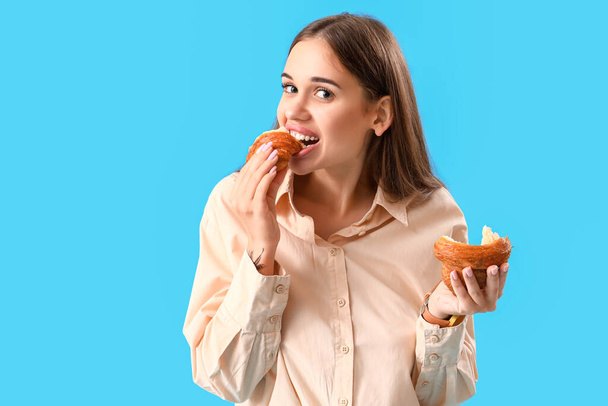 Gyönyörű fiatal nő eszik ízletes croissant kék háttér - Fotó, kép