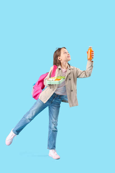 gelukkig klein meisje met fles sap en lunchbox op blauwe achtergrond - Foto, afbeelding