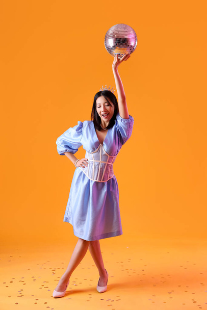 Feliz mujer asiática joven de moda con bola disco sobre fondo naranja - Foto, imagen