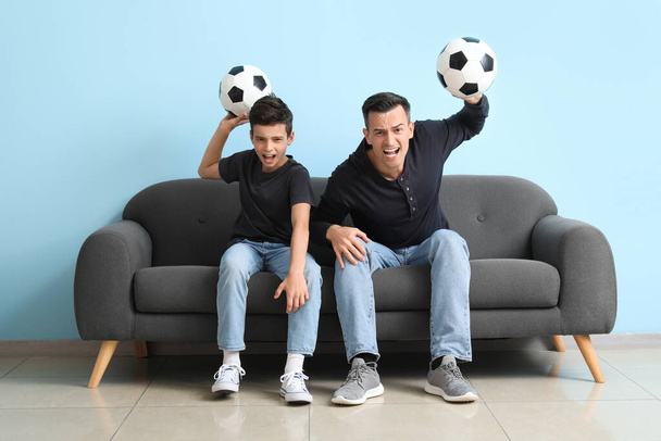 Enojado niño con su padre viendo el partido de fútbol en el sofá cerca de la pared azul - Foto, Imagen