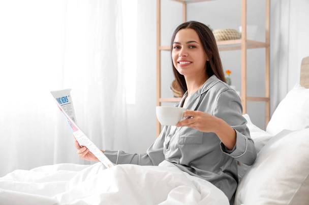 Aamulla kaunis nainen juo kahvia ja lukee sanomalehteä sängyssä - Valokuva, kuva