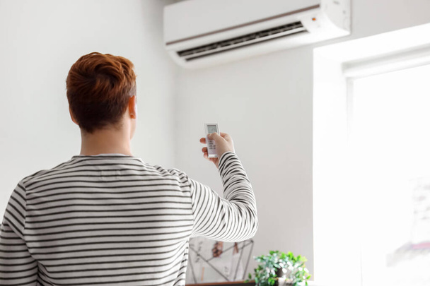 Fiatal férfi bekapcsolása légkondicionáló otthon, visszapillantás - Fotó, kép