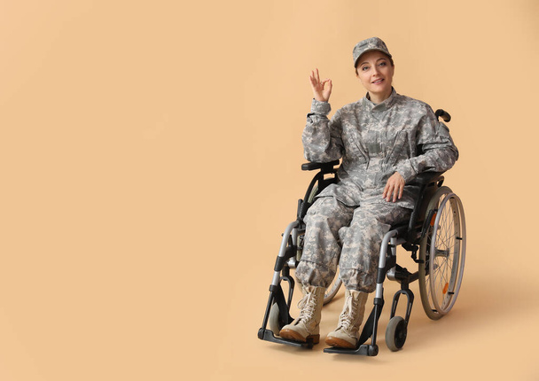 Žena voják na invalidním vozíku ukazuje OK na béžovém pozadí - Fotografie, Obrázek