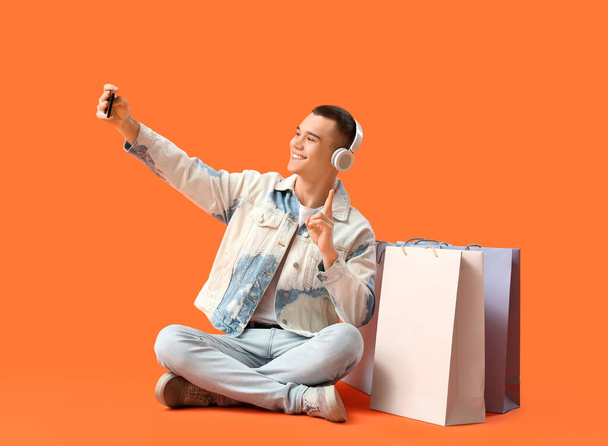 Молодой человек в наушниках с пакетами для покупок делает селфи на красном фоне - Фото, изображение