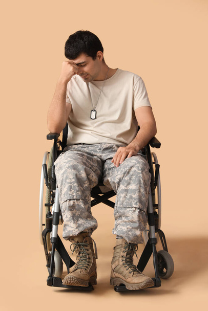 Droevige jonge soldaat in rolstoel op beige achtergrond - Foto, afbeelding