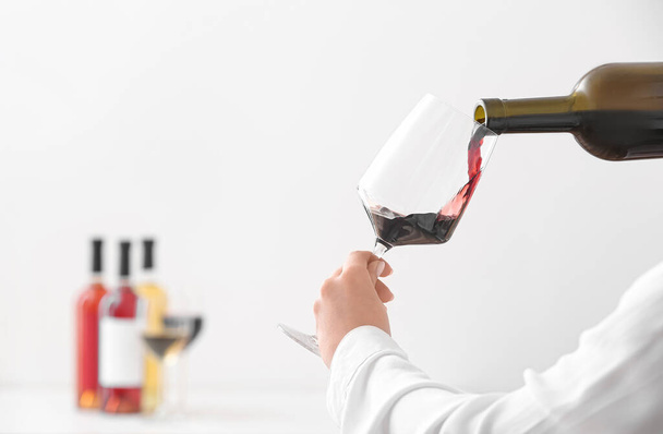 Woman pouring exquisite red wine from bottle into glass on light background - Photo, Image
