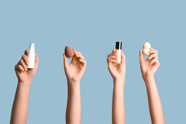 Жіночі руки з губками для макіяжу та пляшками фундаменту на синьому фоні - Фото, зображення