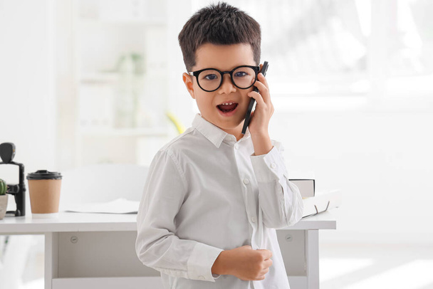Милый маленький бизнесмен разговаривает по мобильному телефону в офисе - Фото, изображение