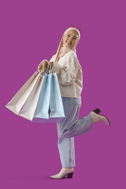 Young Muslim woman with shopping bags on purple background - Photo, Image