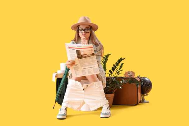 Female traveler reading newspaper on toilet bowl against yellow background - Photo, Image