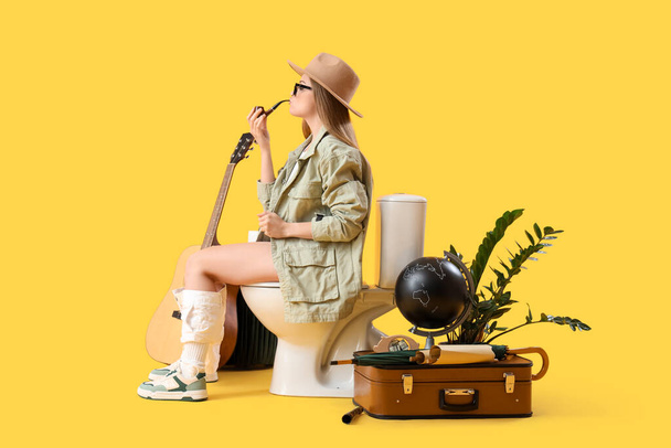 Nainen matkustava tupakointi putki istuu wc kulhoon keltaista taustaa vasten - Valokuva, kuva
