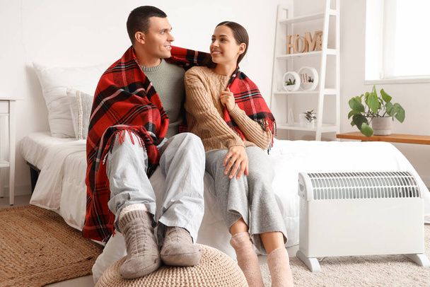 Young couple with plaid warming near radiator in bedroom - Photo, Image