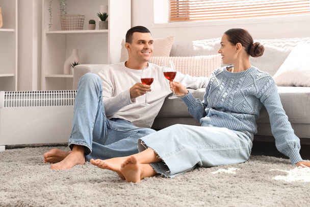 Young couple with wine warming near radiator at home - Photo, Image