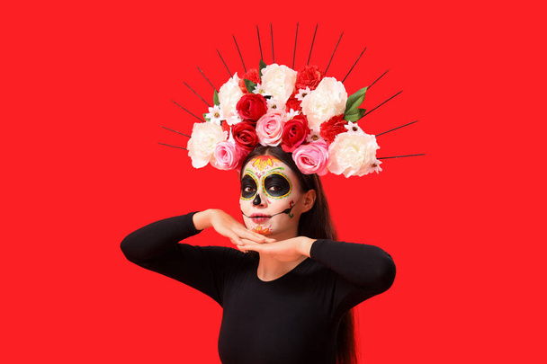 Young woman with painted skull on red background. Mexico's Day of the Dead (El Dia de Muertos) celebration - Photo, Image