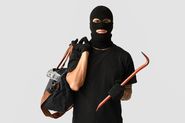 Muž zloděj s páčidlem a taškou peněz na šedém pozadí - Fotografie, Obrázek