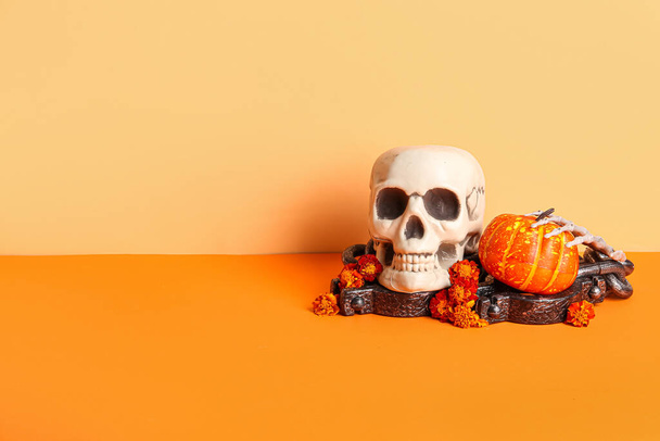Human skull with marigold flowers, pumpkin, skeleton hand and chain on color background - Photo, Image