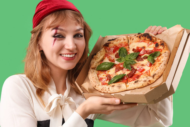 Jeune femme habillée pour Halloween en pirate avec une délicieuse pizza sur fond vert, gros plan - Photo, image