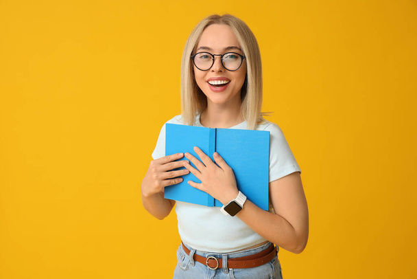 Schöne junge Frau mit Buch auf gelbem Hintergrund - Foto, Bild