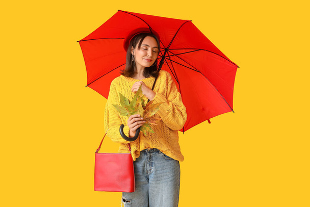 Bella giovane donna con foglie autunnali e ombrello su sfondo giallo - Foto, immagini