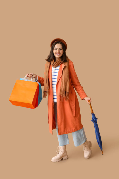 Young woman with shopping bags and umbrella on brown background - Photo, Image