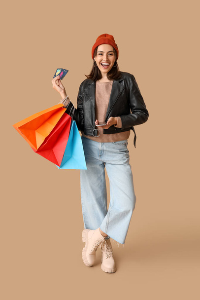 Νεαρή γυναίκα με τσάντες για ψώνια, πιστωτικές κάρτες και κινητό τηλέφωνο σε καφέ φόντο - Φωτογραφία, εικόνα