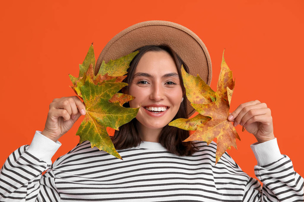 Beautiful young woman with autumn leaves on red background - Photo, Image