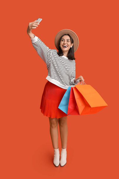 Νεαρή γυναίκα με σακούλες για ψώνια που βγάζει selfie σε κόκκινο φόντο - Φωτογραφία, εικόνα