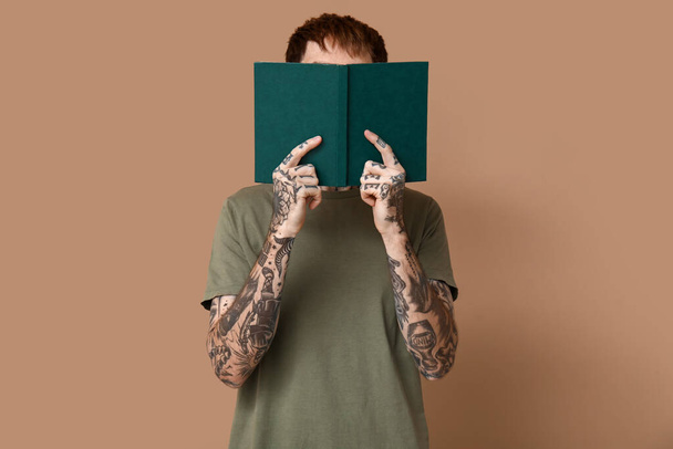 Молодой татуированный мужчина с книгой на коричневом фоне - Фото, изображение