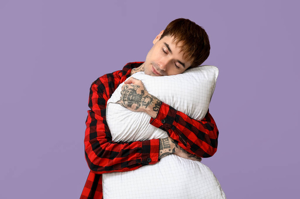 Tatuado jovem em pijama com travesseiro no fundo roxo - Foto, Imagem