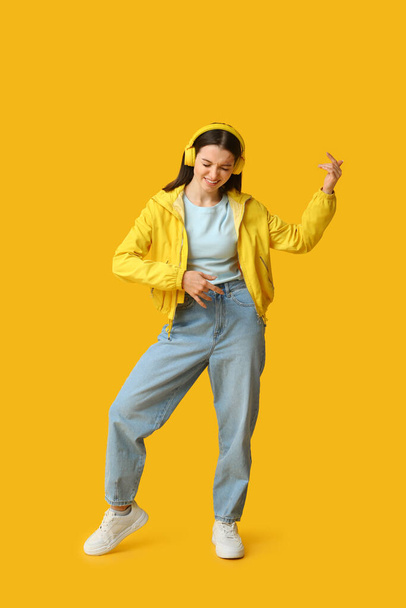 Mujer bastante joven en auriculares tocando guitarra imaginaria sobre fondo amarillo - Foto, Imagen