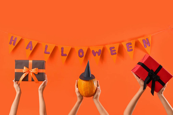 Women with Halloween gifts, pumpkin and flags on orange background - Photo, Image