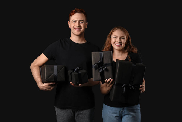 Schönes junges Paar mit Geschenkschachteln auf dunklem Hintergrund. Black-Friday-Verkauf - Foto, Bild