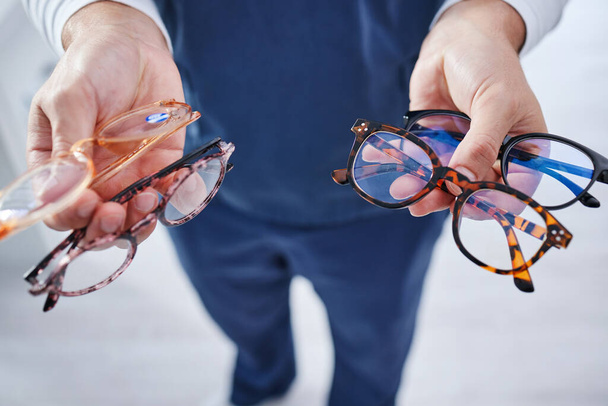 Optometrie, bril en handen van persoon met optie voor frame, voorgeschreven lens en bril voor het zicht. Gezondheidszorg, oogheelkunde en opticien met beslissing voor oogzorg, visie en medische kliniek. - Foto, afbeelding