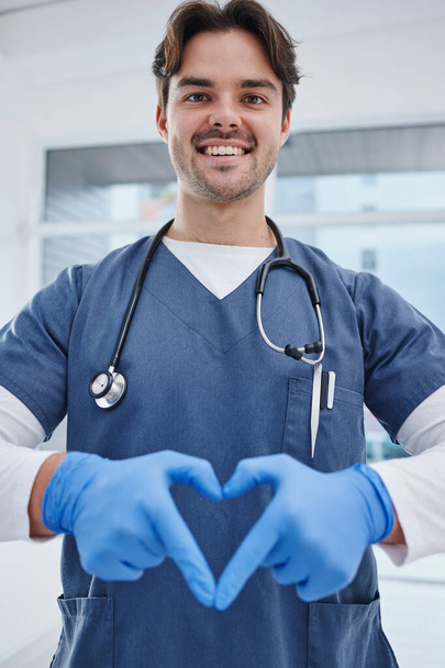 Portrait, hospital and hands in heart of doctor for medicine, surgery and working in clinic for wellness. Healthcare, emoji and man with hand sign for safety, insurance or support for medical service. - Photo, Image