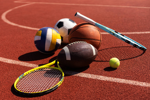 Una variedad de equipos deportivos que incluyen un fútbol americano, una pelota de fútbol, una raqueta de tenis, una pelota de tenis y una pelota de baloncesto. - Foto, Imagen