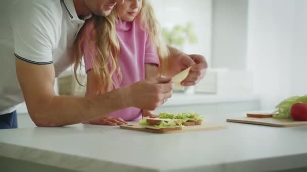 Дружелюбная улыбающаяся дочь с отцом готовит бутерброды на кухне за столом в озорном настроении. Смеющийся папа играет с листом капусты и делает корону в ее голове. Концепция счастья - Кадры, видео