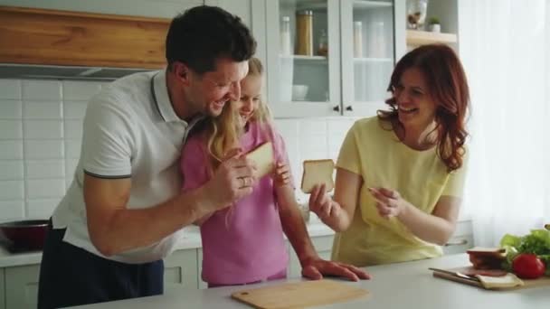 Uma família de sonho americano sorridente positivo na cozinha fazer sanduíches brincalhão. A filha ajuda mamãe e papai a preparar um lanche para um piquenique ou convidados. A demonstração de alimentação saudável. Alto - Filmagem, Vídeo