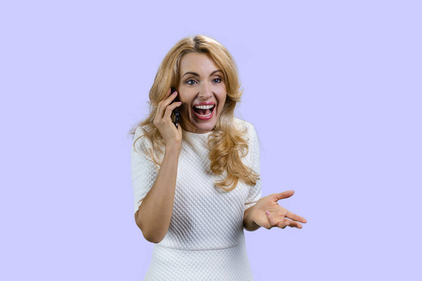Emotional happy mature blonde woman talking on the phone. Isolated on purple. - Photo, Image