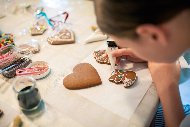 Gros plan d'une jeune fille décorant des biscuits au pain d'épice avec glaçage. - Photo, image