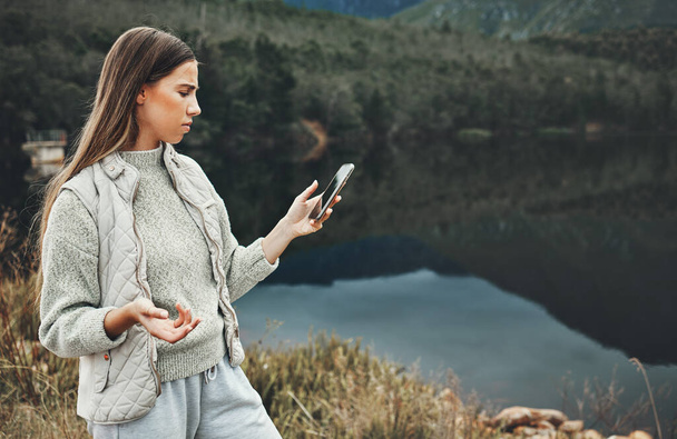 Phone, problem and confused woman hiking by lake in nature, travel or vacation. Smartphone, network error and person outdoor by river trekking, frustrated or bad signal connection, lost or app glitch. - Photo, Image