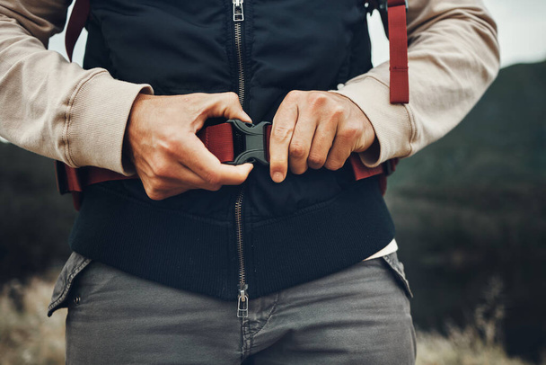 Closeup hands, man and nature fastening a backpack for hiking, trekking or travel in the mountains. Walking, buckle clip and a tourist with a bag in the woods for activity, fitness and exercise. - Photo, Image