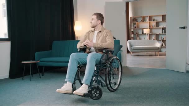 彼の部屋の車椅子に座っている若い白人男性は幸せで満足しています. カメラを見ている障害のある男性 - 映像、動画