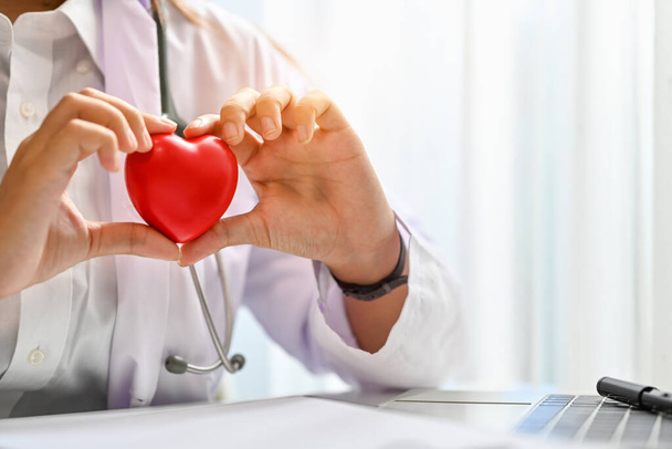 Lääkäri valkoisessa takissa ja stetoskooppi kädessä pitäen sydämen punaista muotoa. Lääkärintarkastus, terveydenhuolto ja lääketieteellinen käsite. - Valokuva, kuva