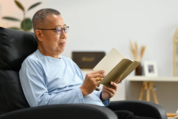 Portré egy pozitív végzősről, aki a karosszéken ül és könyvet olvas. Idős emberek életmód, hobbi és pihenés. - Fotó, kép