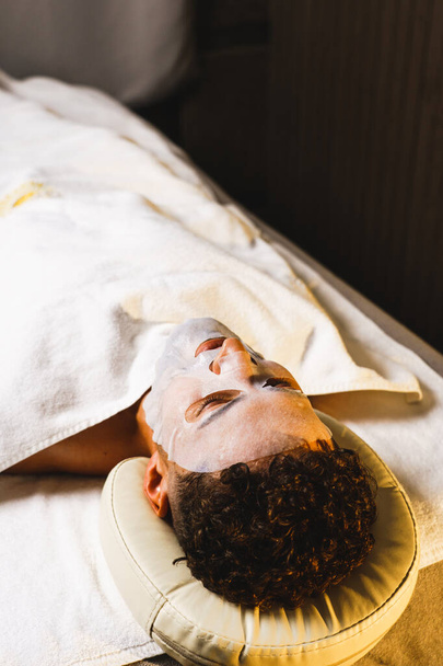 Een man ontspant in een massageruimte voor een gezichtsmassage. Het concept van gezondheid en huidverzorging - Foto, afbeelding