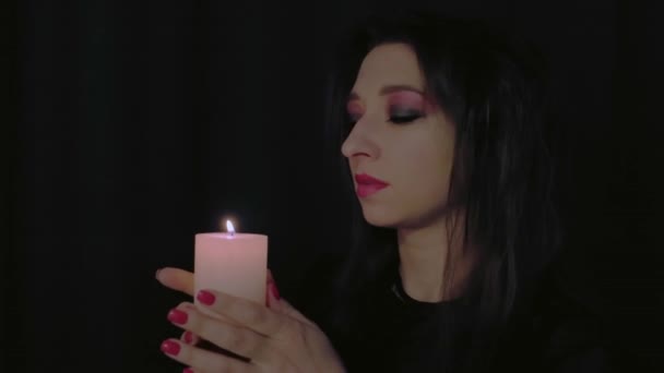 Una chica apaga una vela en la oscuridad. Primer plano de una cara de mujer. Concepto mágico de Halloween. Imágenes de alta calidad 4k - Imágenes, Vídeo