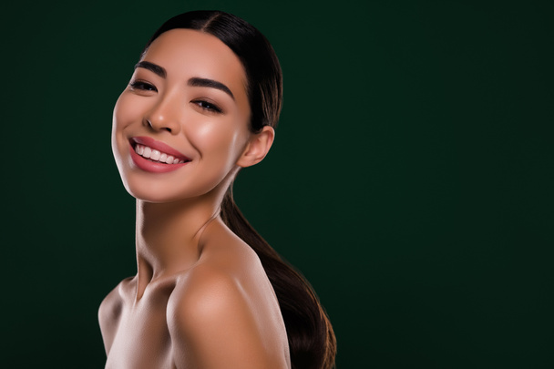 Göz kamaştırıcı Asyalı kadının fotoğrafı. Işıl ışıl gülüyor. Model spa salonunun omuzları izole edilmiş koyu yeşil arka planda.. - Fotoğraf, Görsel