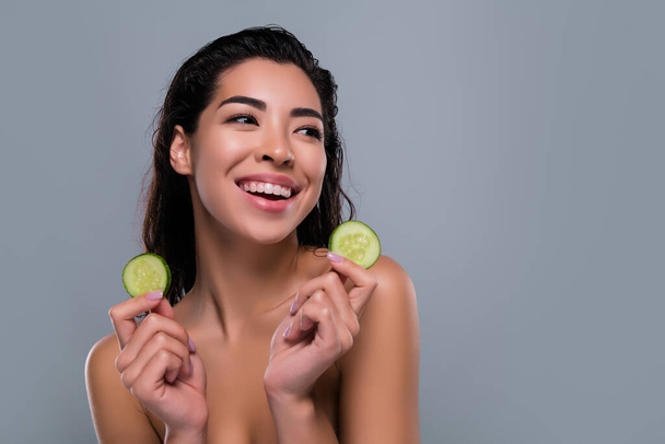 Foto di splendida donna asiatica tenere cetriolo verdura organico spa salone spalle fuori isolato colore grigio sfondo. - Foto, immagini