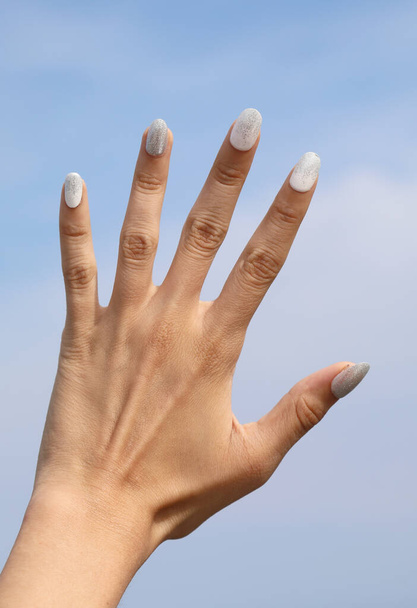 five fingers of the hand with the background of the blue sky and white nail polish on the nails - Photo, Image